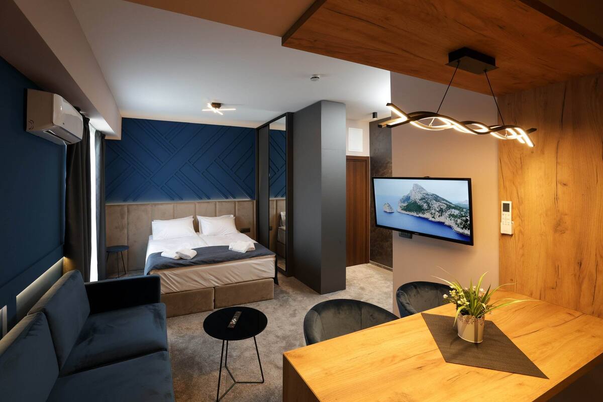 A modern hotel room with a bed, a desk, a TV, and a potted plant.