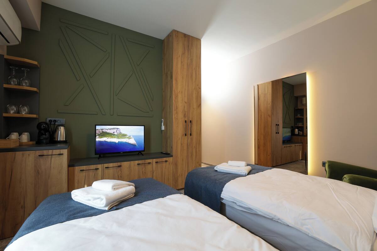 A hotel room with two beds, a television, wooden cabinets, and a green accent wall.