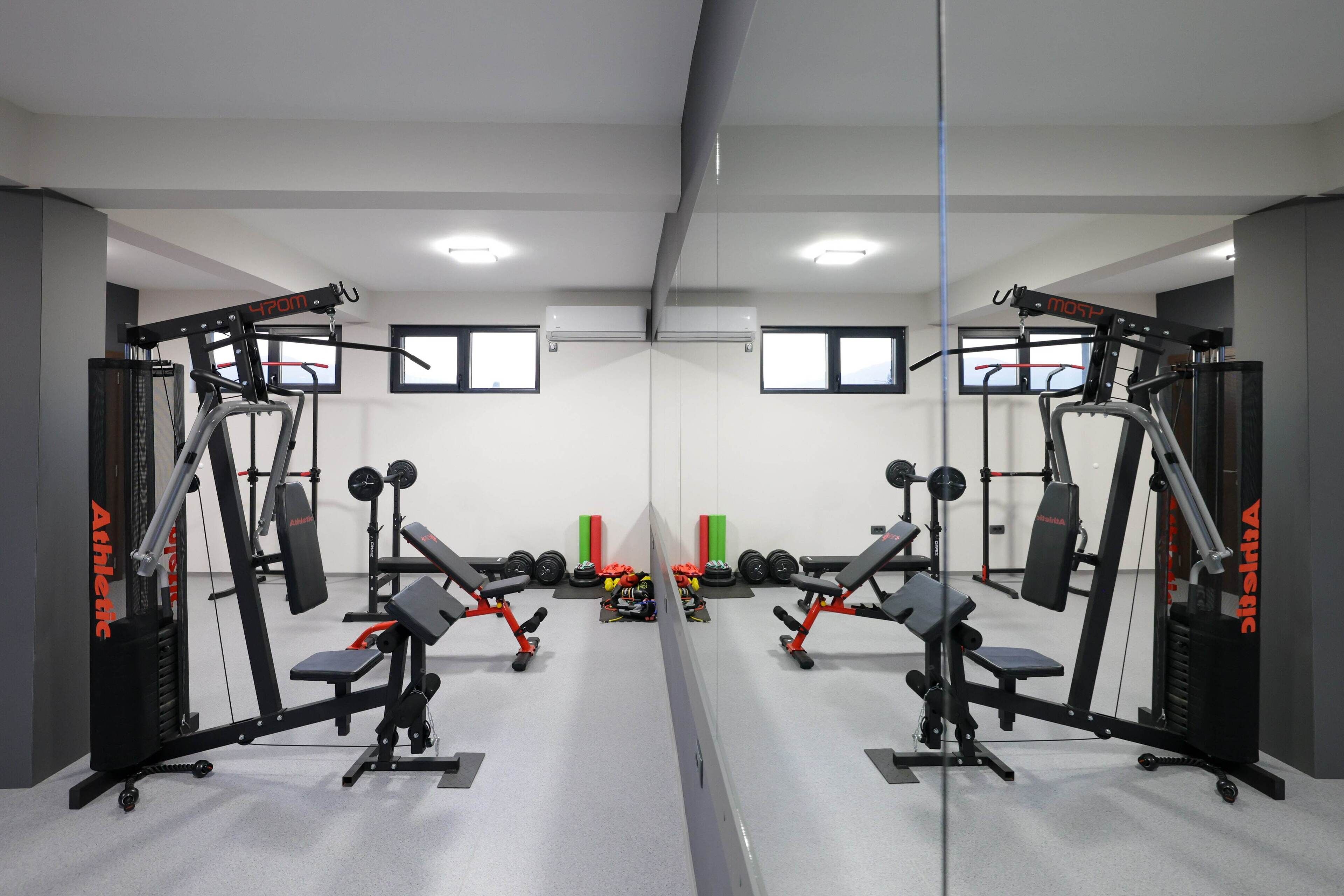 A gym with mirrored walls, weightlifting equipment, and dumbbells.