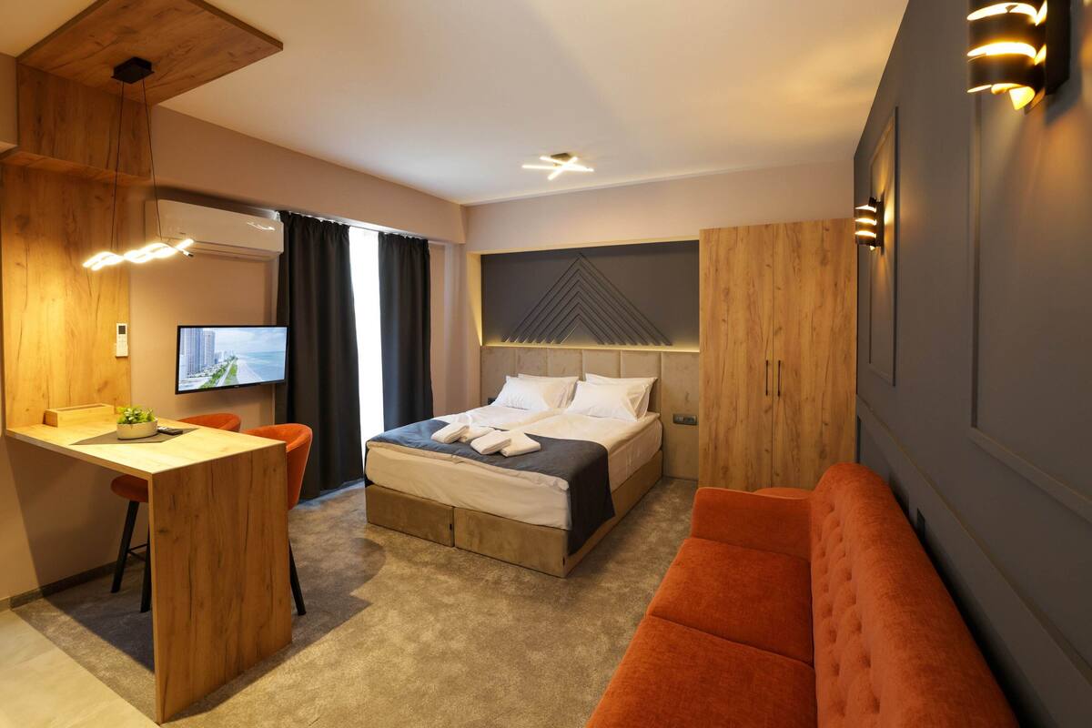 A modern hotel room with a bed, a desk, a chair, and a sofa.