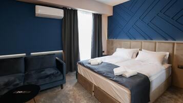 A hotel room with a bed, a sofa, a small table, and a window with curtains.