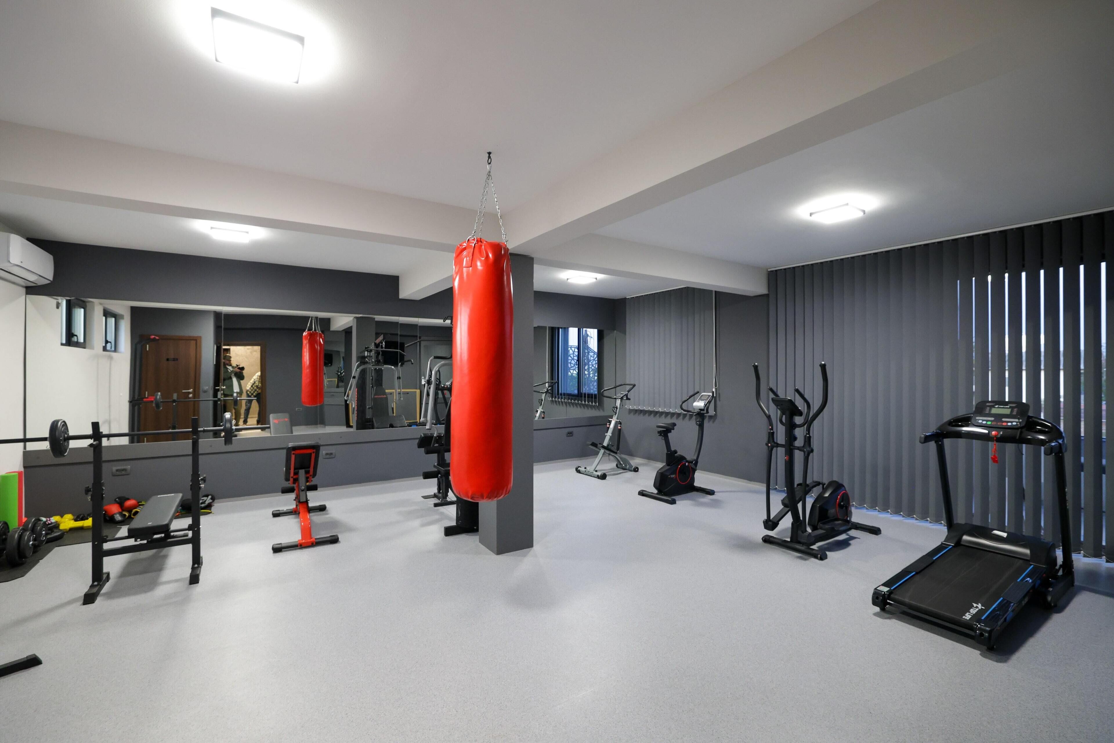 A modern gym with various exercise equipment, including a punching bag, weight bench, and cardio machines.