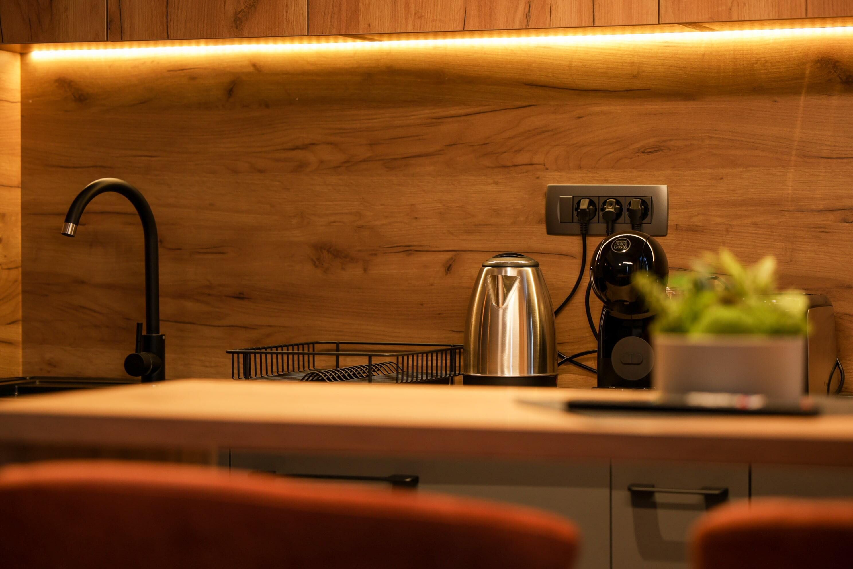 A kitchen with wooden cabinets, a black faucet, a kettle, and a power strip.