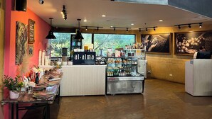 Interno di un caffè con un bancone, scaffali pieni di bevande e opere d'arte alle pareti.