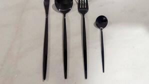 A set of four black cutlery items: a knife, a spoon, a fork, and a teaspoon, arranged on a marble surface. - Depa Privado 2 Hab 5p Santa Tere (Guadalajara)