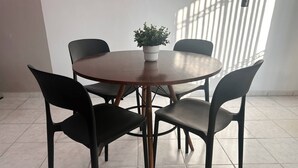 A round wooden table with four black chairs, a potted plant, and a window with vertical blinds. - Depa Privado 2 Hab 5p Santa Tere (Guadalajara)