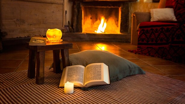 A cozy room with a fireplace, a book, and a candle on a rug.