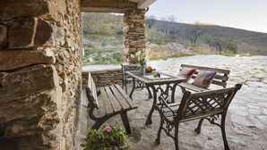 A stone patio with wooden furniture, including a bench and a table with a vase of flowers.