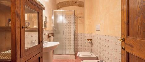 A bathroom with a wooden cabinet, a sink, a toilet, and a shower.