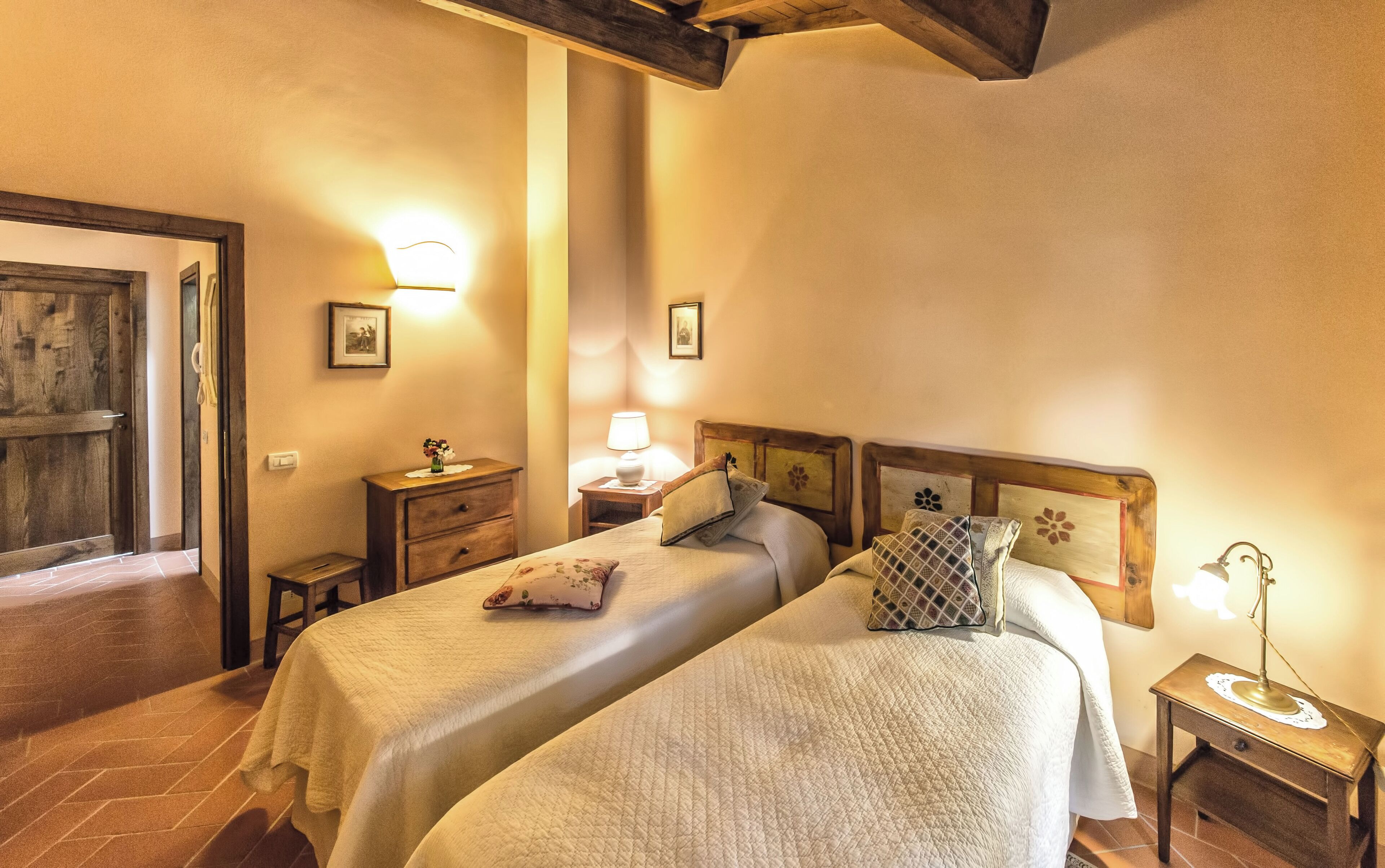 Une chambre d’hôtel avec deux lits, une tête de lit en bois, des tables de chevet avec des lampes et une porte donnant sur une autre pièce.