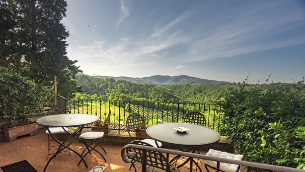 Una terraza con dos mesas redondas y sillas, con vistas a un paisaje verde exuberante y colinas distantes.