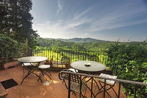 A terrace with two round tables and chairs, overlooking a lush green landscape and distant hills.