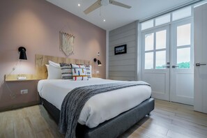 Une chambre à coucher avec un lit, des lampes de chevet, une décoration murale en macramé, un tableau encadré et une grande fenêtre.