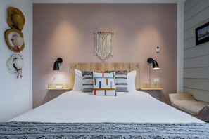 A neatly made bed with a headboard, two bedside lamps, and a macrame wall hanging.