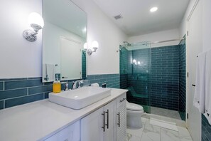 Une salle de bain moderne avec un meuble-lavabo blanc, une douche en verre et un grand miroir agrémenté d’appliques murales.