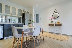 Une cuisine moderne avec des armoires blanches, un four encastré et un coin repas comprenant une table et des chaises blanches.