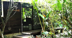 A rustic wooden cabin with a small porch, surrounded by dense tropical vegetation.