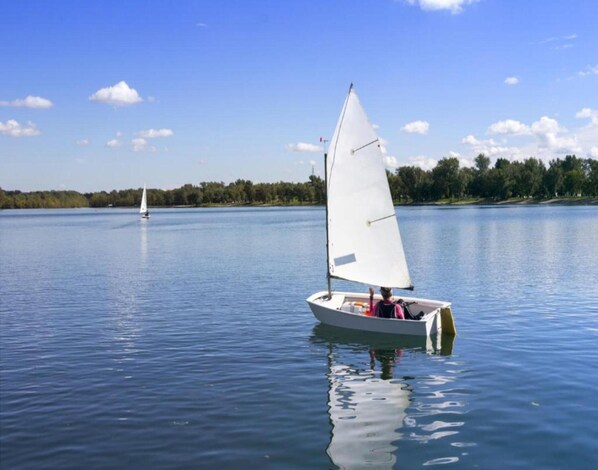 A calm lake with a sailboat in the foreground and another in the distance.