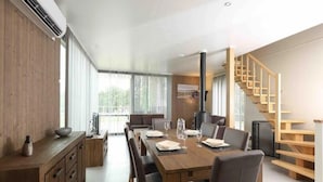 A modern dining area with a wooden table, chairs, and a built-in stove. - Serene Luxe Lakeside Stay (Froidchapelle)