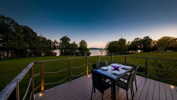 A deck with a table and chairs overlooking a lake at dusk. - Serene Luxe Lakeside Stay (Froidchapelle)