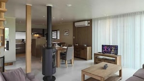 A modern living room with a sofa, a coffee table, and a TV. There is a kitchen in the background with a dining area. - Serene Luxe Lakeside Stay (Froidchapelle)