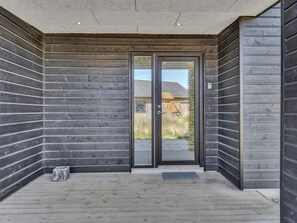 A modern building entrance with a glass door, a concrete ceiling, and a wooden deck.