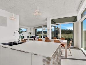 A modern kitchen with a large island, dining area with chairs, and a view through glass doors.