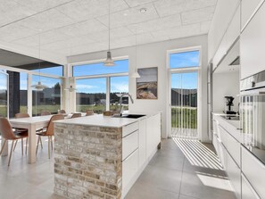 A modern kitchen with a large island, white cabinetry, and a view of the outdoors.