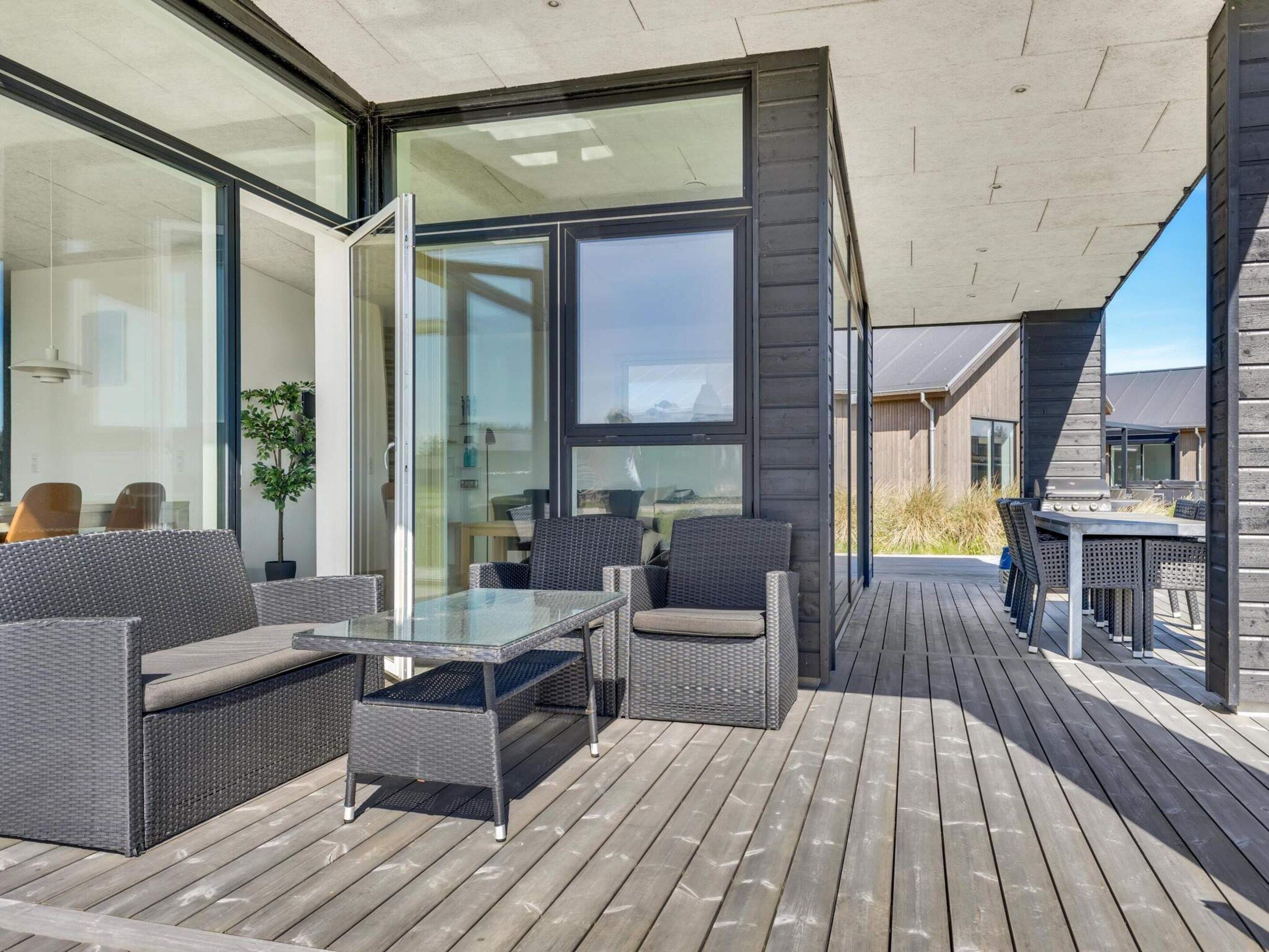 Eine moderne Terrasse im Freien mit Korbmöbeln, Glastischen und Blick auf die umliegende Landschaft.