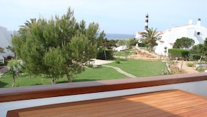 Eine Holzterrasse mit Blick auf eine Küstenlandschaft, einschließlich eines Leuchtturms und weißer Gebäude.