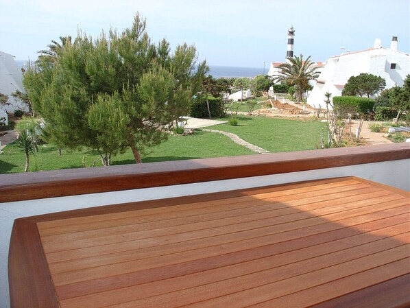 Un muelle de madera con vistas a un paisaje costero, que incluye un faro y edificios blancos.