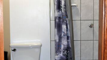A bathroom with a toilet, a shower with a patterned curtain, and a window with a view of greenery.