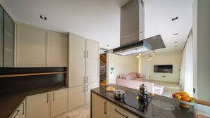 Eine moderne Küche mit hellen Schränken, einer dunklen Arbeitsplatte und einem eingebauten Herd. Es gibt einen Essbereich mit einem rosafarbenen Sofa und einem an der Wand befestigten Fernseher.
