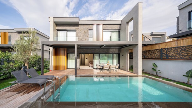 Ein modernes, zweistöckiges Haus mit Swimmingpool, Außenmöbeln und einer überdachten Terrasse.