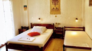 A room with two single beds, a wooden headboard, a bedside table, a wall tapestry, and a window with curtains. - Southern Crete, Filoxenia Villa, is a group of ten holiday apartments (Koutsounari)