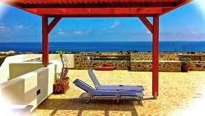 A red pergola with two striped lounge chairs on a tiled patio overlooking the sea. - Southern Crete, Filoxenia Villa, is a group of ten holiday apartments (Koutsounari)