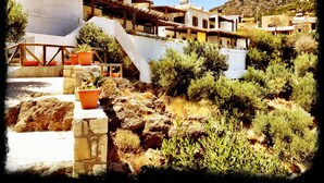 A traditional Mediterranean-style building with a white facade, terracotta roof tiles, and a red lattice window. - Southern Crete, Filoxenia Villa, is a group of ten holiday apartments (Koutsounari)