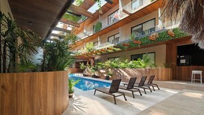 Ein mehrstöckiger Innenbereich mit Pool, Liegestühlen und viel Grün.