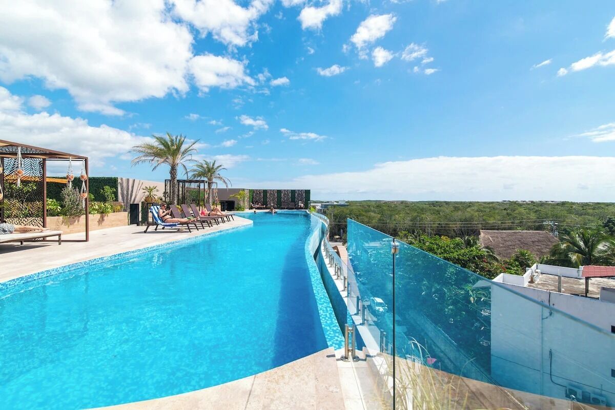 A swimming pool with lounge chairs and a pergola, surrounded by greenery and a clear sky.