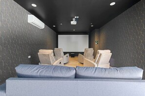 A room with a projector screen, reclining chairs, a sofa, and a wall-mounted air conditioner. - Vibra Bonito Luxe Boho-chic Hideaway in Tulum (Tulum)