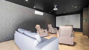 A modern cinema room with a grey patterned wall, a large screen, and reclining chairs.