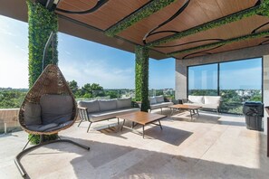 A rooftop terrace with a hanging chair, sofas, and a table, surrounded by greenery and large windows. - Vibra Bonito Luxe Boho-chic Hideaway in Tulum (Tulum)