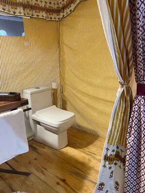 A small, compact bathroom with a toilet, a wooden floor, and striped wallpaper. - Kumbh Travel (Prayagraj)