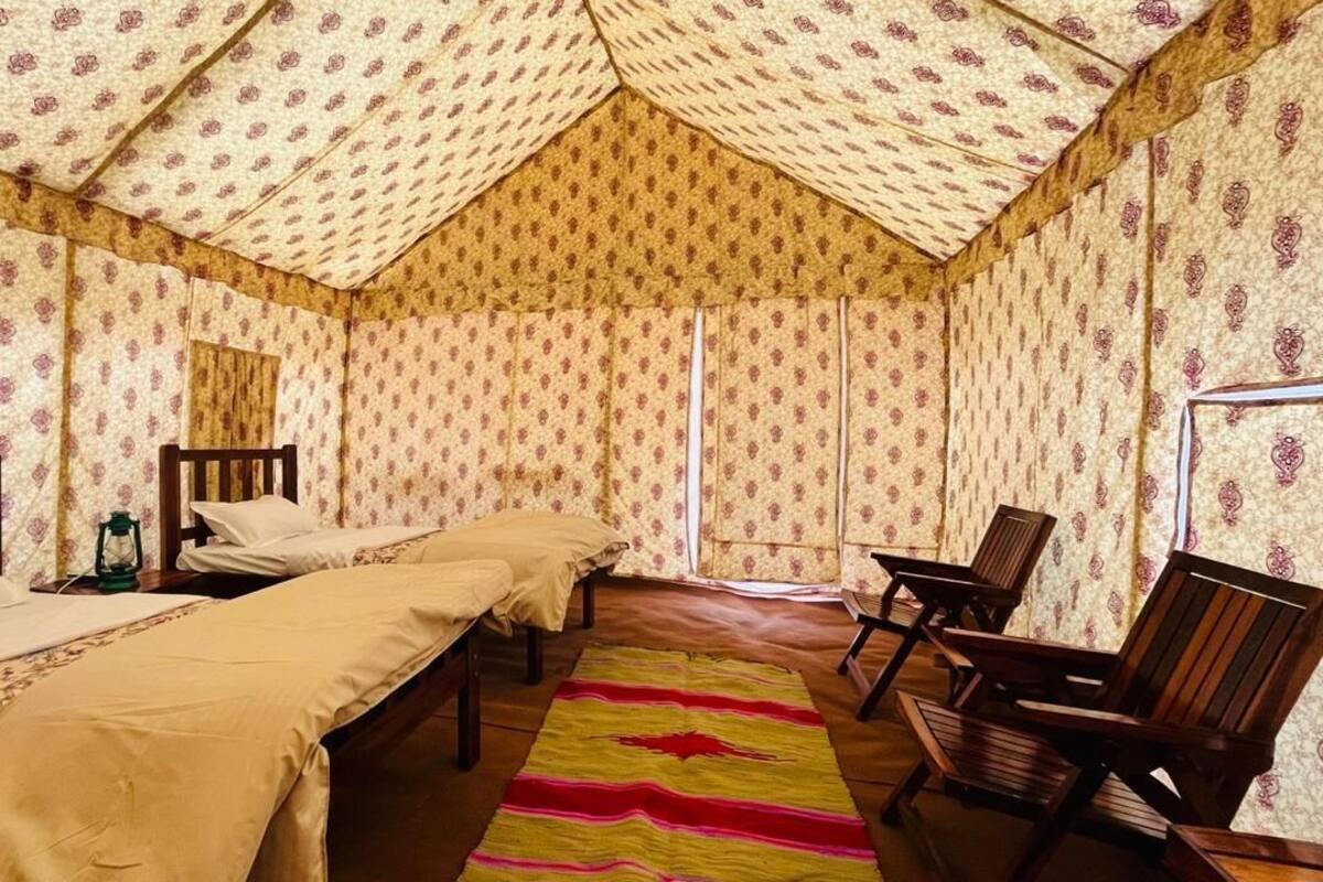 A room with two beds, a wooden chair, a small table, and a patterned wall.