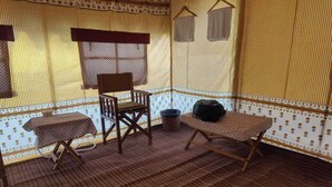 A room with a patterned carpet, a wooden table, a chair, and a small stool. - Kumbh Travel (Prayagraj)
