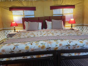 A double bed with floral bedding, two bedside lamps, and a window with a striped curtain. - Kumbh Travel (Prayagraj)