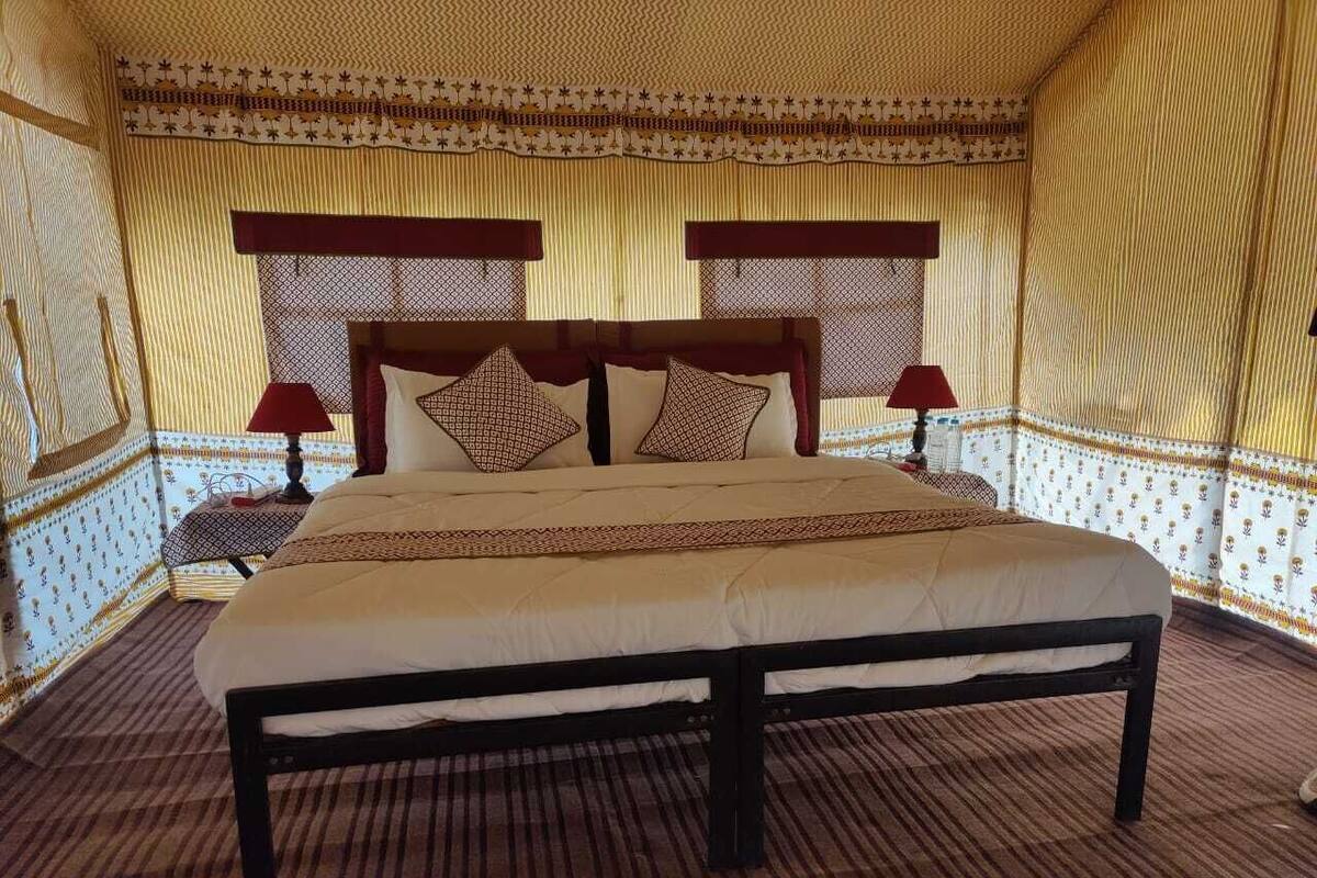 A large bed with a wooden frame and white bedding, flanked by two nightstands with lamps, in a room with patterned walls and a striped carpet.