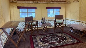 A cozy room with a patterned wall, a wooden table, two chairs, a small table with a tray, and a decorative rug. - Kumbh Travel (Prayagraj)