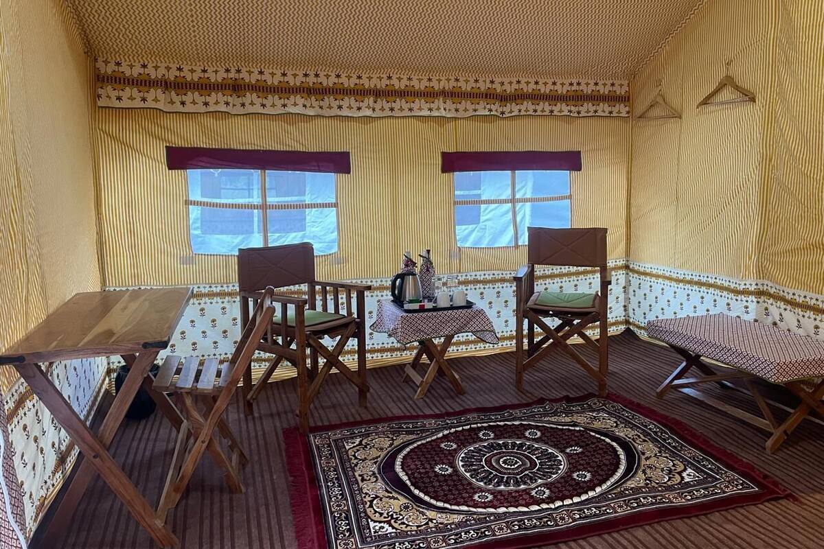 A cozy room with a patterned wall, a wooden table, two chairs, a small table with a tray, and a decorative rug.
