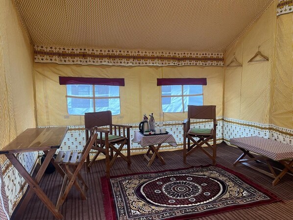 A cozy room with a patterned wall, a wooden table, two chairs, a small table with a tray, and a decorative rug. - Kumbh Travel (Prayagraj)